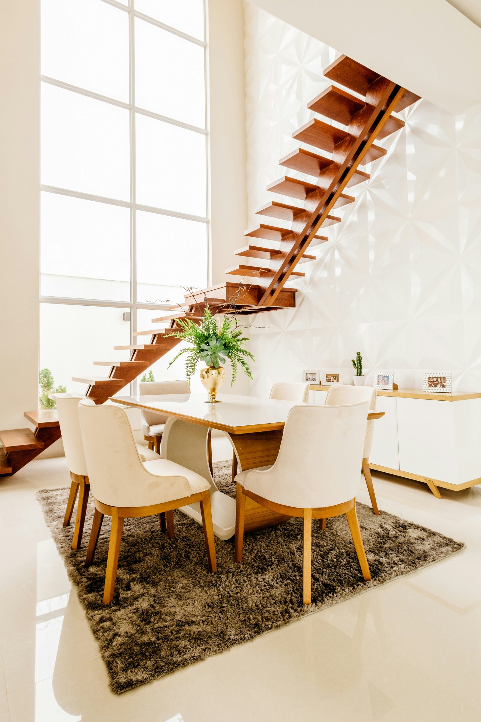 Escalier suspendu en bois menant à l'étage, au-dessus d'une salle à manger baignée de lumière naturelle